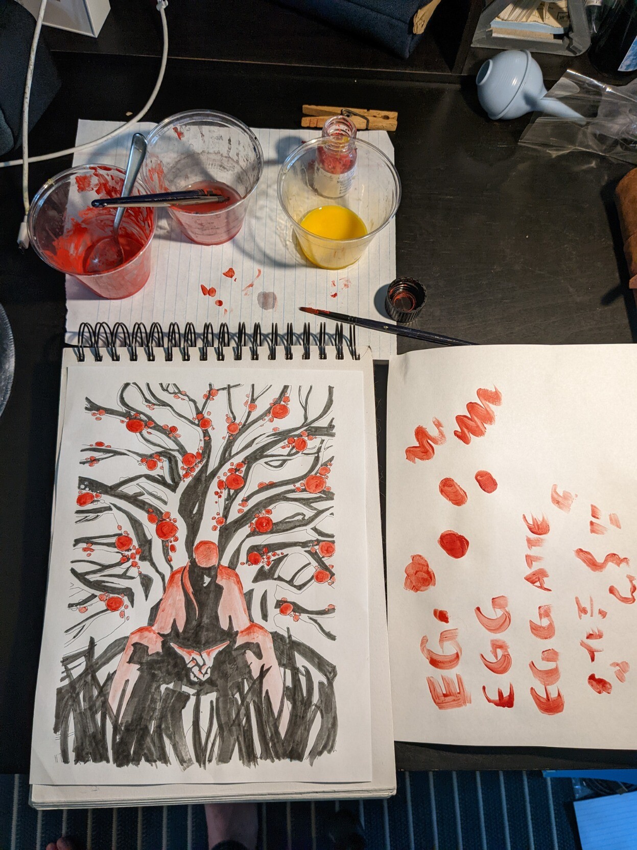 A mess of a work station, including plastic cups of water, egg, and pigment, a piece of scrap paper that says EGG, and the finished painting.