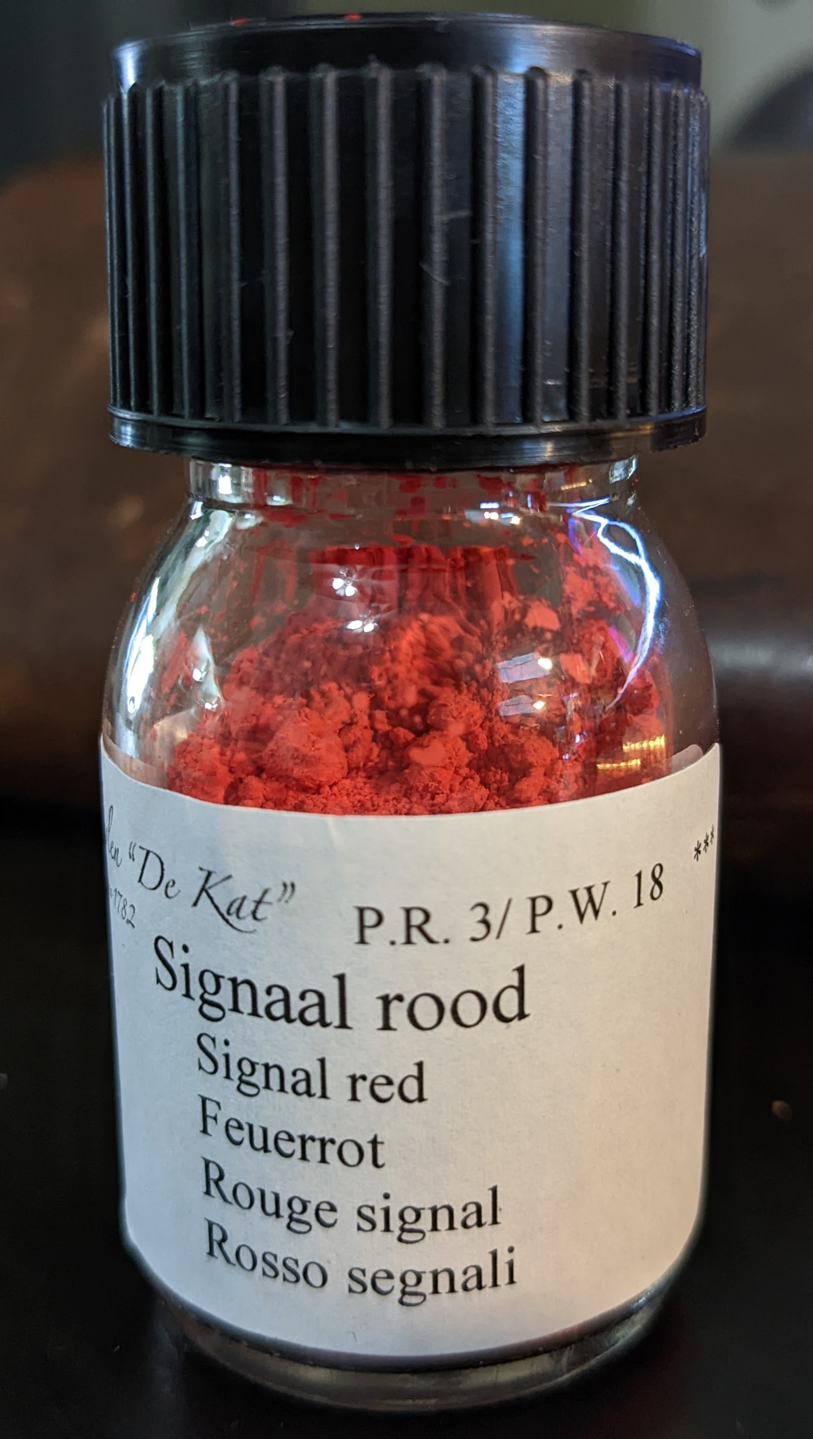 a small plastic jar of red pigment, says 'Signal rood'